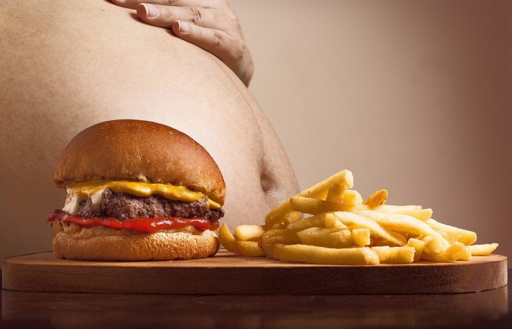 An obese man's belly next to some frieds and a hamburger.