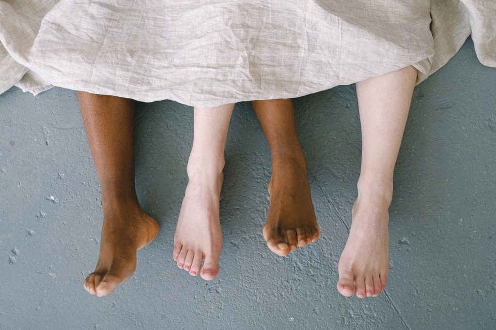Bare feet of a man and a woman coming out of the bed sheets.